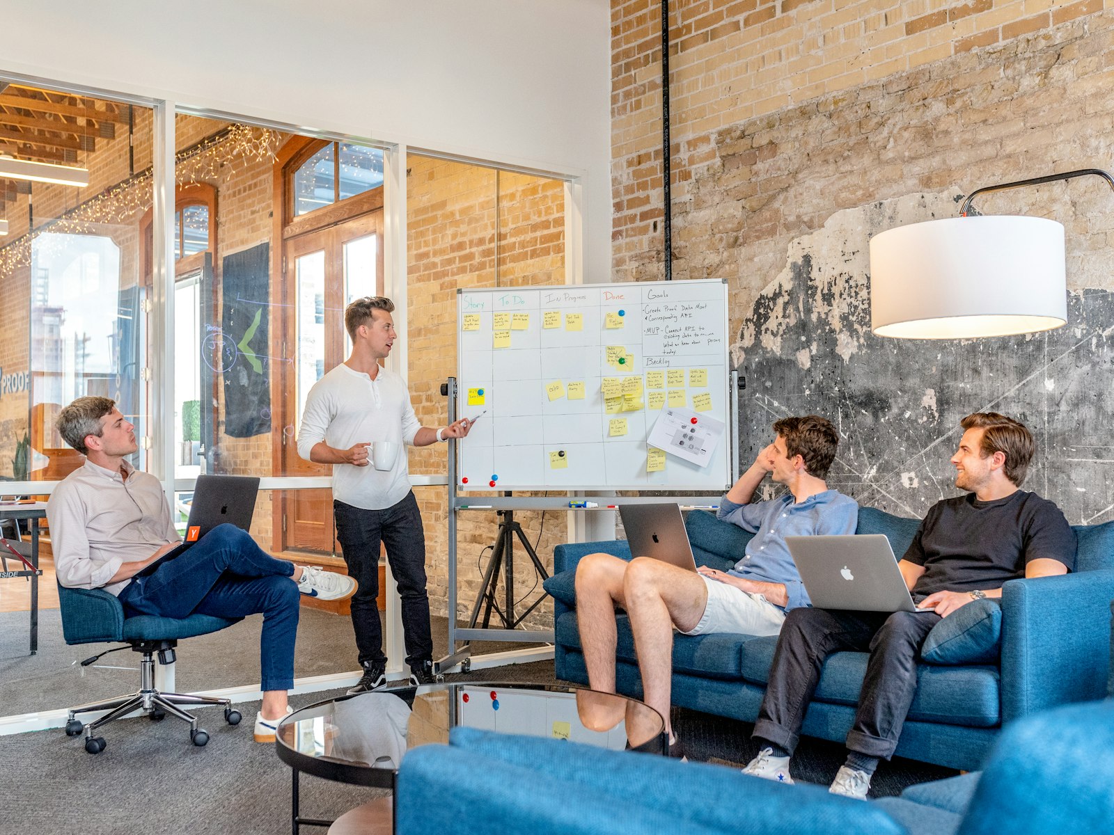 marketing team at laptops watching a colleague present workflow strategy at a whiteboard